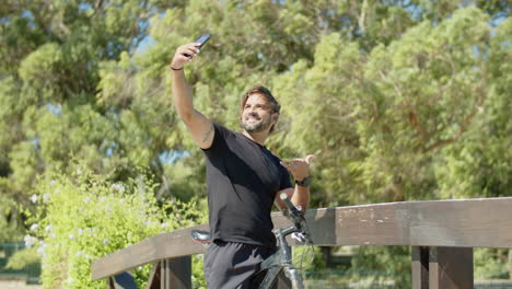 Vertikale-Bewegung-Eines-Bikers,-Der-Im-Sommerpark-Ein-Selfie-Mit-Dem-Telefon-Macht